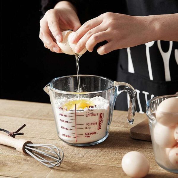 Person cracking an egg into a glass measuring cup filled with flour.