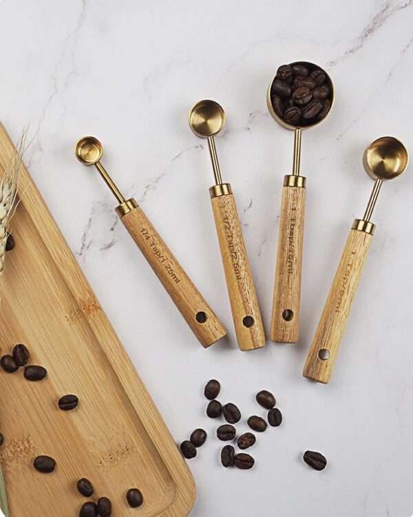 A picture of four small measuring spoons with wooden handles arranged neatly on a white marble table, with a visible wooden board on the side. One of the spoons contains coffee beans, adding a touch of contrast and texture to the composition.