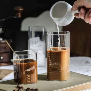 Three transparent drinking glasses on a table, filled with rich coffee, while a person pours milk into one of the glasses.