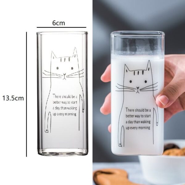 A picture of a person holding a drinking glass with a cute cat design printed on it. Below the cat, there is a motivational quote that reads 'There should be a better way to start a day than waking up every morning.’ The glass contains milk and on the other side, clear measurements are displayed.