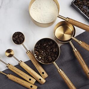 A picture featuring a set of four big golden measuring cups with wooden handles, accompanied by a set of four small golden measuring spoons with wooden handles. One of the measuring cups contains coffee beans, while another holds flour, and the remaining two are empty. One of the measuring spoons contains coffee beans, while the other is empty, and the other two are not visible in the picture.